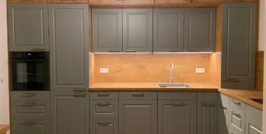 Küchenstudio Moderne Küche mit grauen Schränken, Arbeitsflächen und Aufkantung aus Holz, eingebautem Backofen, Spüle, Unterschrankbeleuchtung und einer Katze, die in der unteren linken Ecke auf dem Boden sitzt.