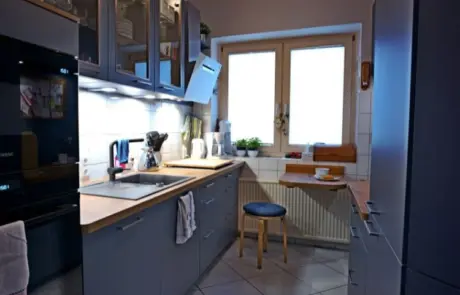 Küchenstudio Moderne Küche mit blauen Schränken, einer Arbeitsplatte aus Holz, einem eingebauten Ofen, einer Spüle, Unterschrankbeleuchtung und einem kleinen Sitzbereich an zwei großen Fenstern.