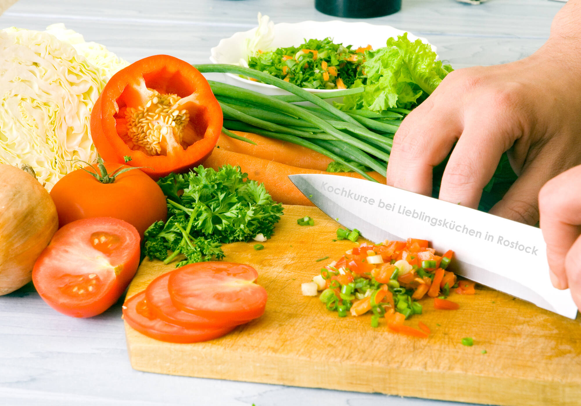 Küchenstudio Eine Person schneidet Gemüse, darunter Tomaten und grüne Zwiebeln, auf einem Holzbrett, umgeben von frischem Gemüse, während eines Kochabends für Frauen mit Krebs in einer einladenden Küche. Küchenstudio Eine Person schneidet Gemüse, darunter Tomaten und grüne Zwiebeln, auf einem Holzbrett, umgeben von frischem Gemüse, während eines Kochabends für Frauen mit Krebs in einer einladenden Küche.