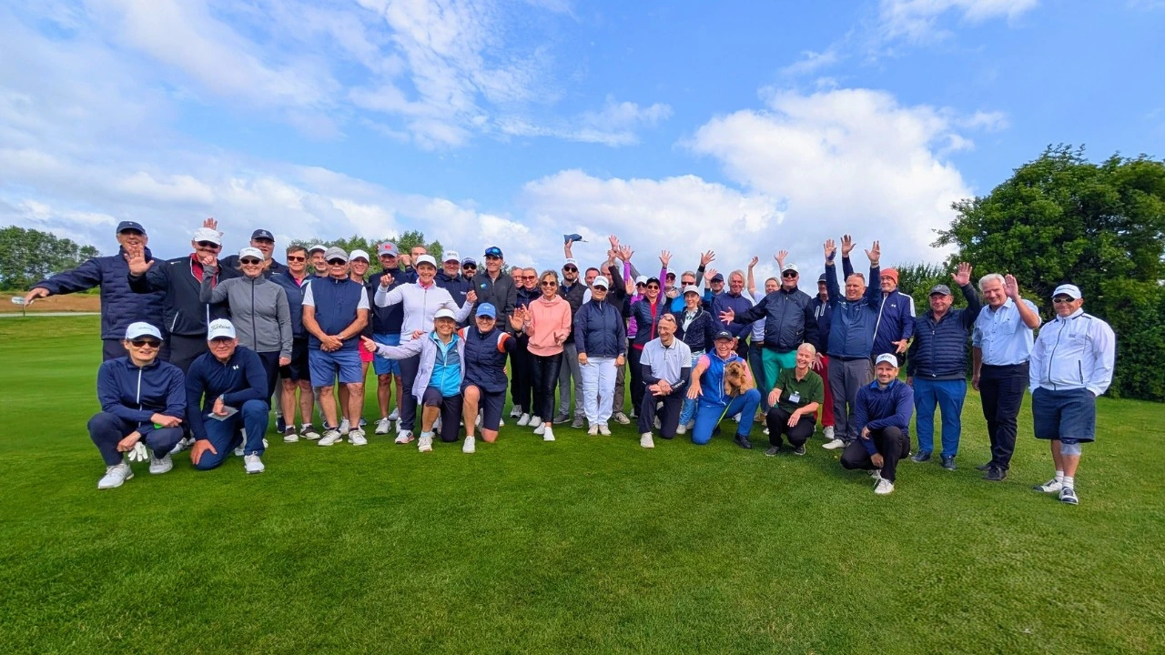 Küchenstudio Eine große Gruppe von Menschen posiert gemeinsam auf einem Golfplatz während eines Charity-Golfturniers; viele lächeln und strecken die Arme in die Höhe, während der Himmel teilweise bewölkt ist.