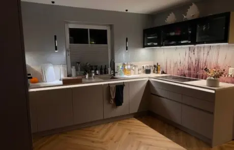 Küchenstudio Moderne Küche mit L-förmigen Arbeitsflächen, Holzboden, Unterbauleuchten, einem Fenster über der Spüle und einer dekorativen Fliesenwand mit hohen Grashalmen und zwei weißen abstrakten Formen an den Oberschränken. Küchenstudio Moderne Küche mit L-förmigen Arbeitsflächen, Holzboden, Unterbauleuchten, einem Fenster über der Spüle und einer dekorativen Fliesenwand mit hohen Grashalmen und zwei weißen abstrakten Formen an den Oberschränken.