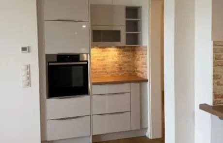 Küchenstudio Eine kompakte Küchenzeile mit integriertem Backofen, hellen Schränken, einer Arbeitsplatte aus Holz und einer Küchenrückwand im Ziegelstein-Look.