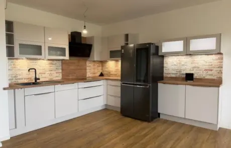 Küchenstudio L-förmige Küche mit weißen Schränken, Arbeitsplatten aus Holz, einer Küchenrückwand im Ziegelstil und einem schwarzen Kühlschrank.
